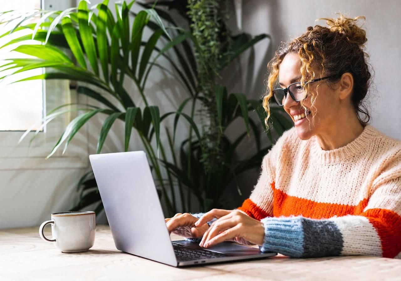 A smiling woman sitting in front of a laptop, figuring out how much does it cost to start a clothing brand.